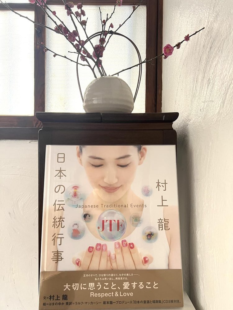 Un ejemplar de Japanese Traditional Events (JTE) sobre un atril de madera en casa de Shoko Shiraishi, con ramas de ciruelo en flor dispuestas en un jarrón de cerámica de Hagi. Fotografía de enero de 2024.